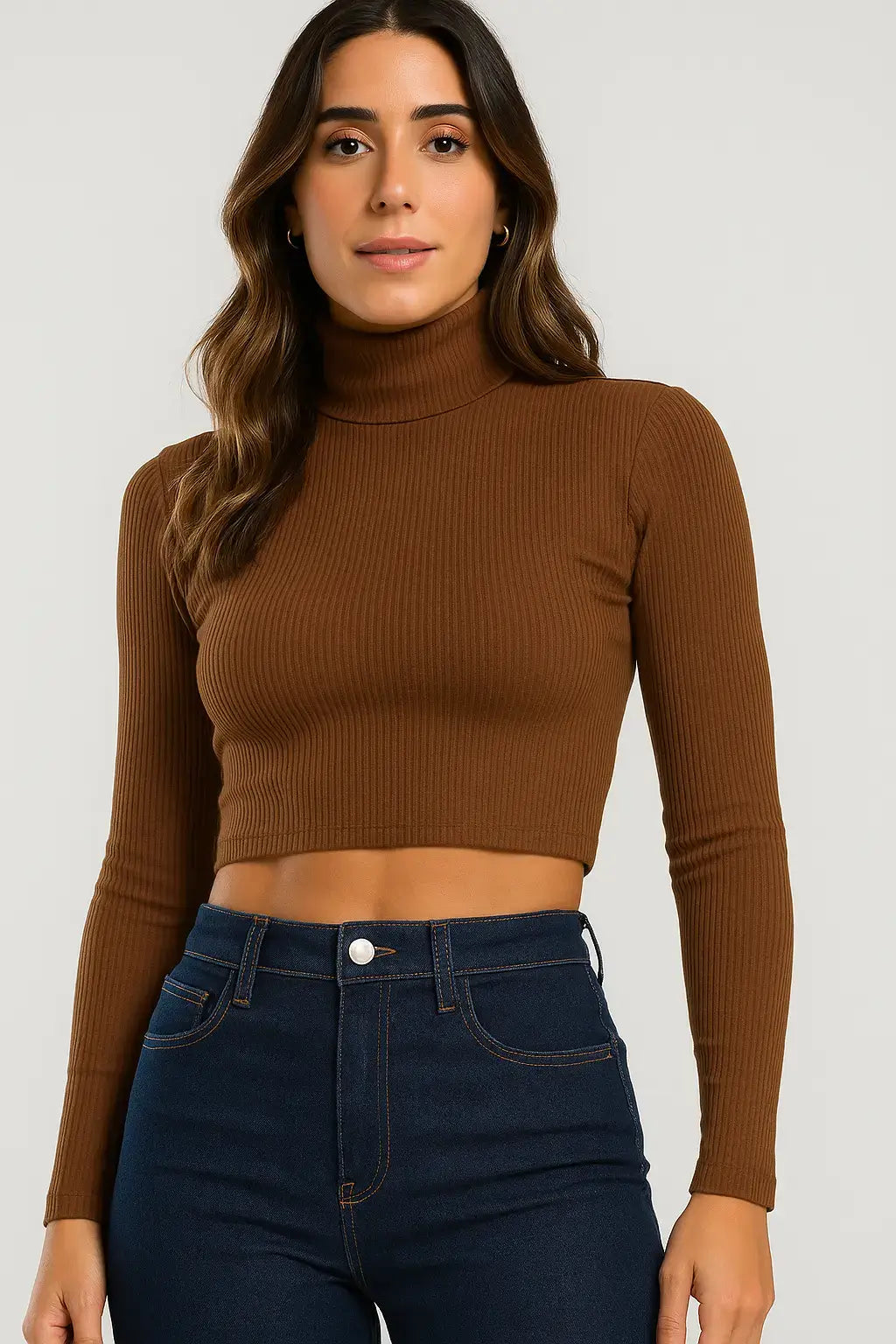 Mulher vestindo blusa cropped canelada marrom de manga longa com gola alta, combinada com calça jeans de cintura alta, em fundo neutro.