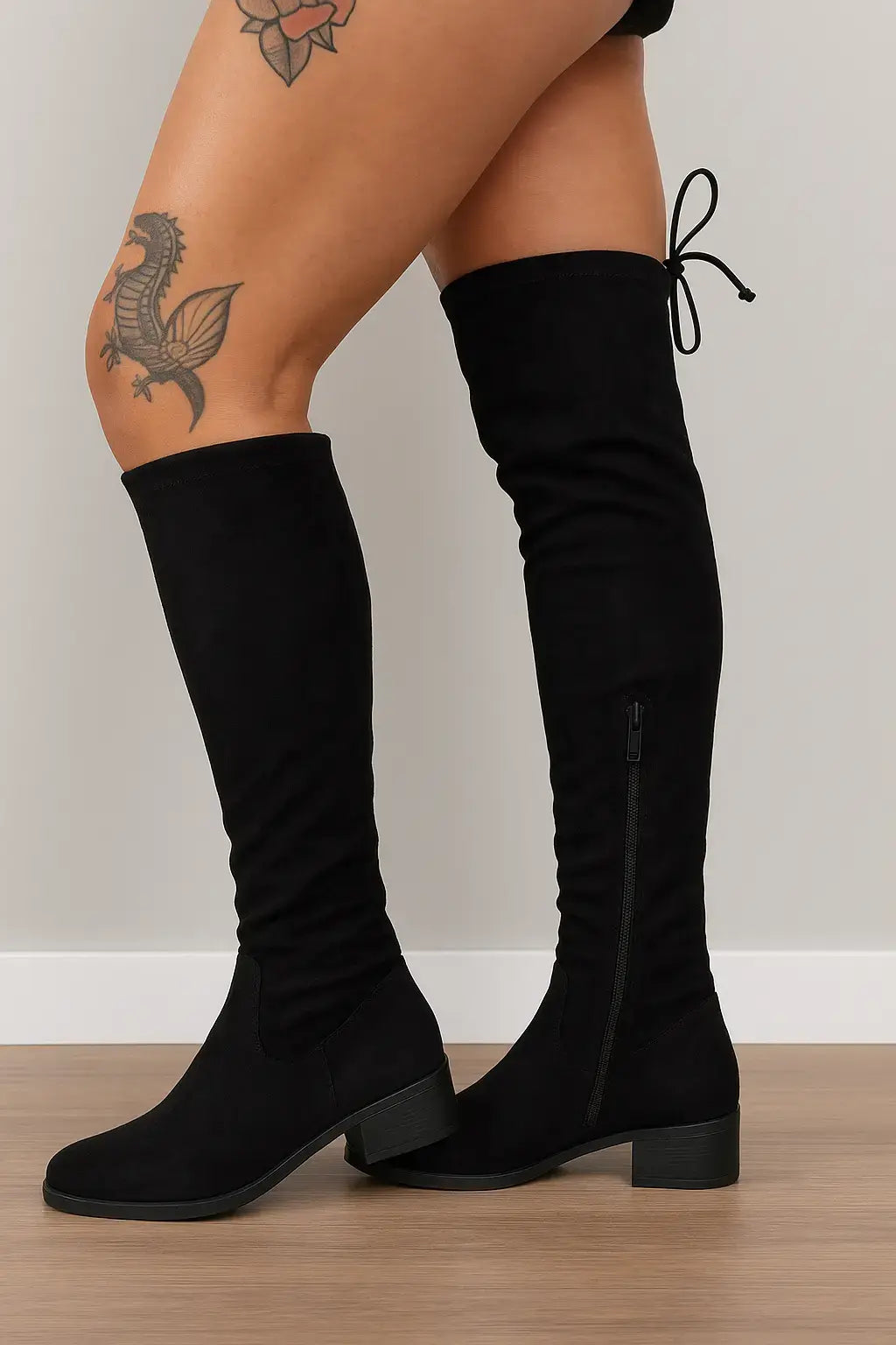 Mulher usando bota over the knee preta com salto baixo e amarração traseira, ideal para compor looks modernos e confortáveis no inverno.