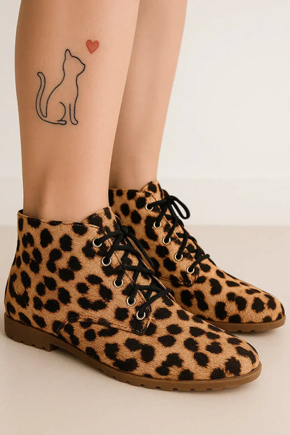 Mulher com bota feminina de estampa onça, cano curto e cadarço preto, destacando tatuagem de gato com coração na perna.