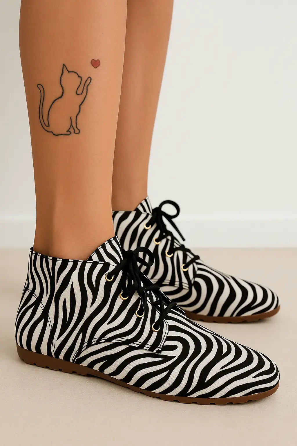 Mulher com bota feminina estampada de zebra em preto e branco, cano curto com cadarço, exibindo tatuagem de gato com coração na perna.