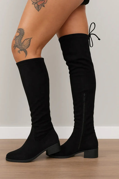 Mulher usando bota over the knee preta com salto baixo e amarração traseira, ideal para compor looks modernos e confortáveis no inverno.