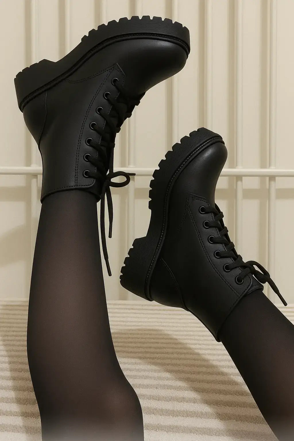 Coturno feminino preto com cano curto e sola tratorada, estilo plataforma, usado com meia-calça preta, em fundo claro com grade metálica vertical.