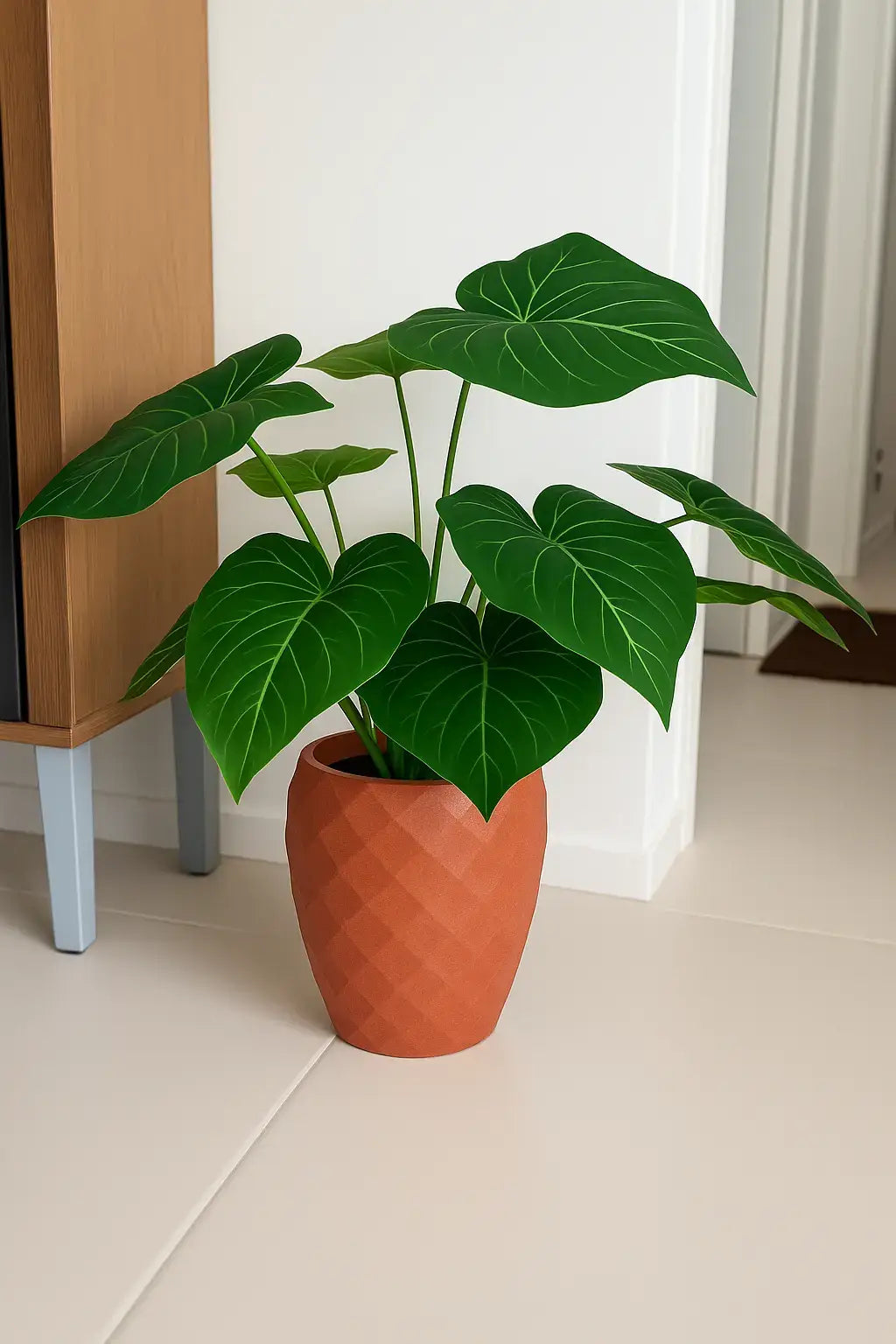 Planta artificial tipo Alocasia com folhas verdes em vaso terracota com textura geométrica, perfeita para decoração de interiores modernos.