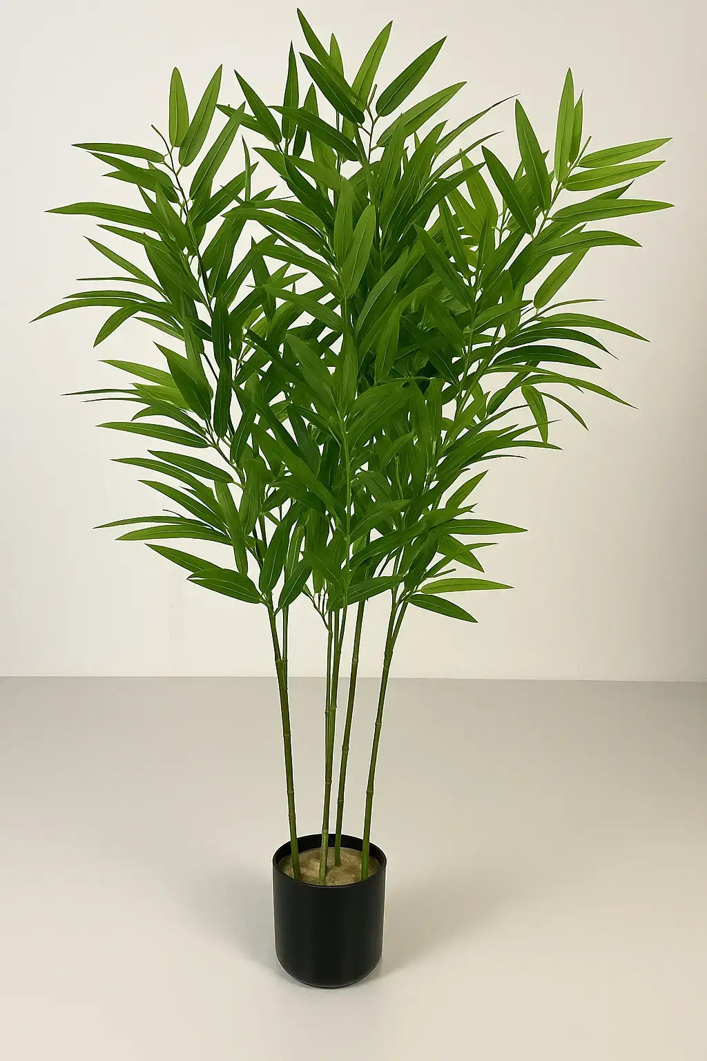 Planta de bambu artificial com folhagem densa em vaso preto cilíndrico sobre piso claro, ideal para ambientes internos com decoração clean e moderna.