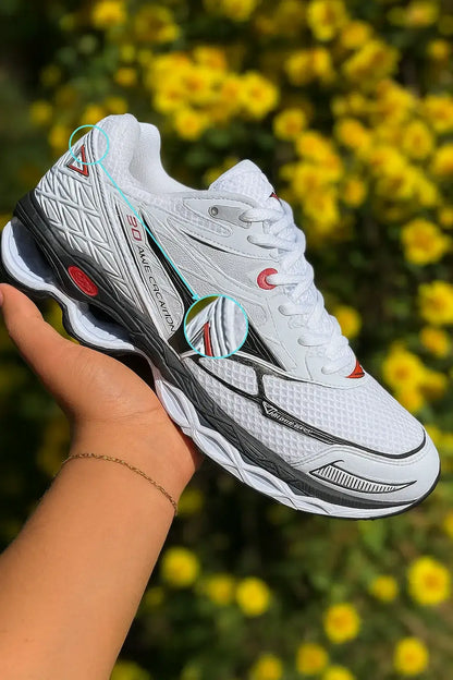 Tênis MZ Wave Creation 20 branco com detalhes em preto e vermelho sendo exibido na mão, com fundo de flores amarelas desfocadas, ideal para corrida e conforto diário.